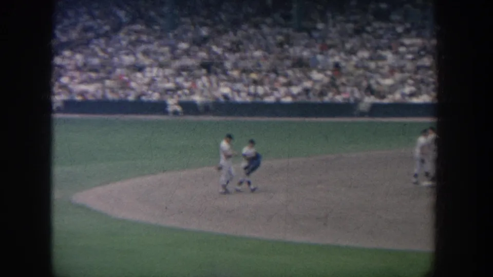 1964 New York stadium baseball scene with players and a dark-clad official or catcher near the infield before packed stands.