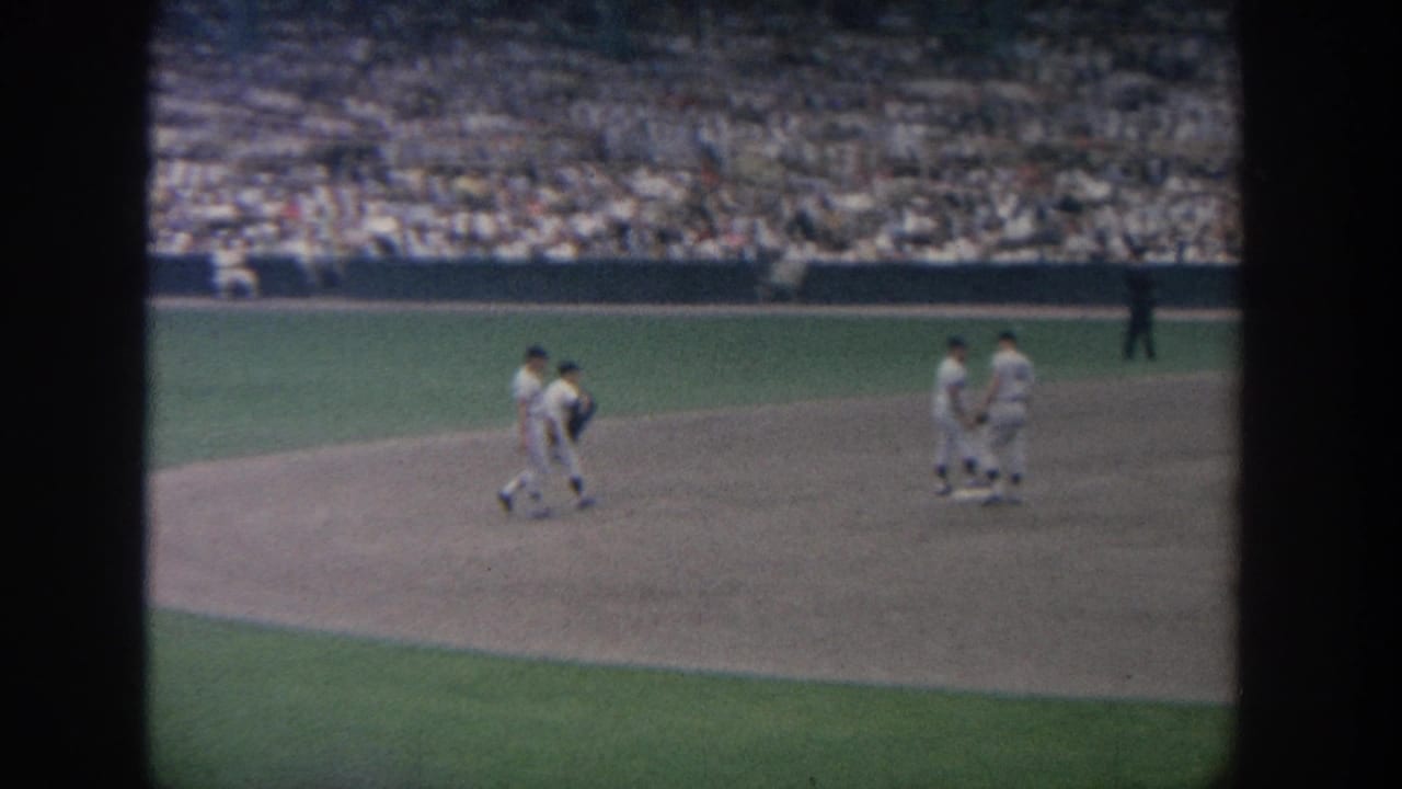 1964 New York 8mm footage shows baseball players in white uniforms walking across the infield with crowded stands behind them.