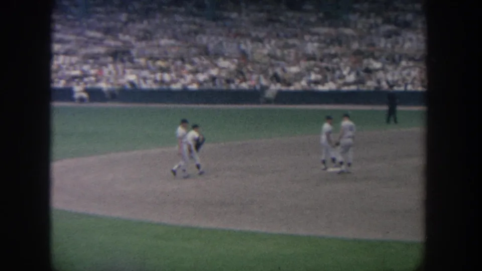 1964 New York 8mm footage shows baseball players in white uniforms walking across the infield with crowded stands behind them.