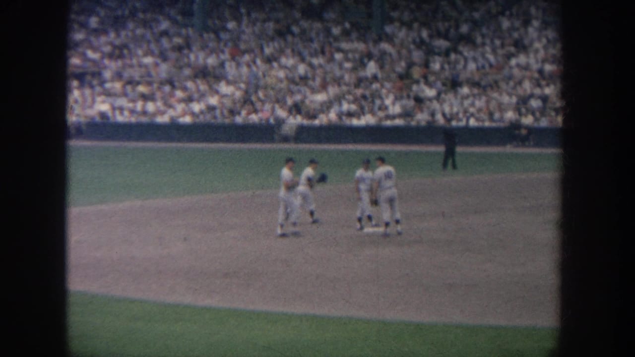 Several baseball players gather on the infield with a large crowd in the stands.