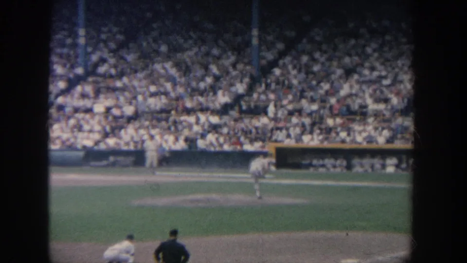 1964 New York 8mm frame shows a pitcher completing or preparing a pitch while other field figures remain visible near the infield.