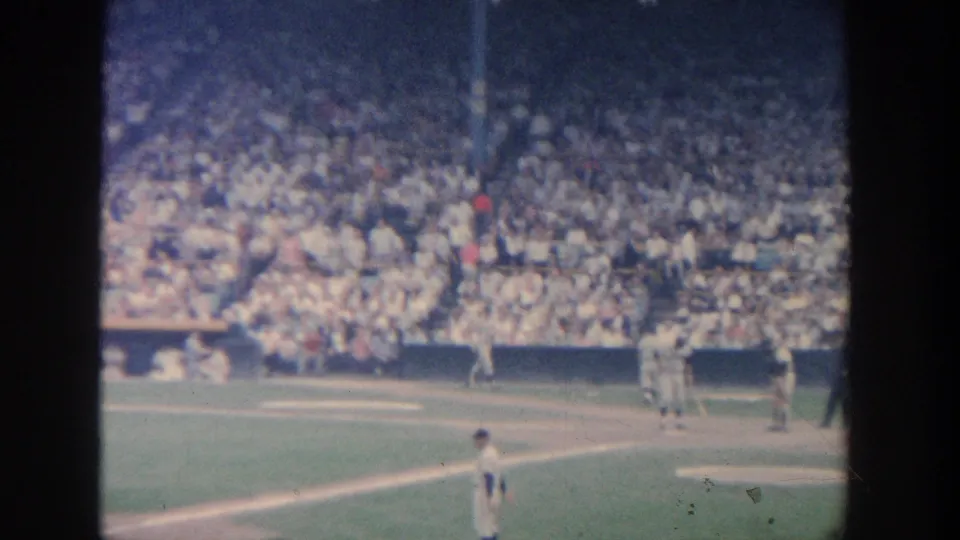1964 New York 8mm frame showing fielders around the infield and a packed stadium crowd, framed by dark film edges.