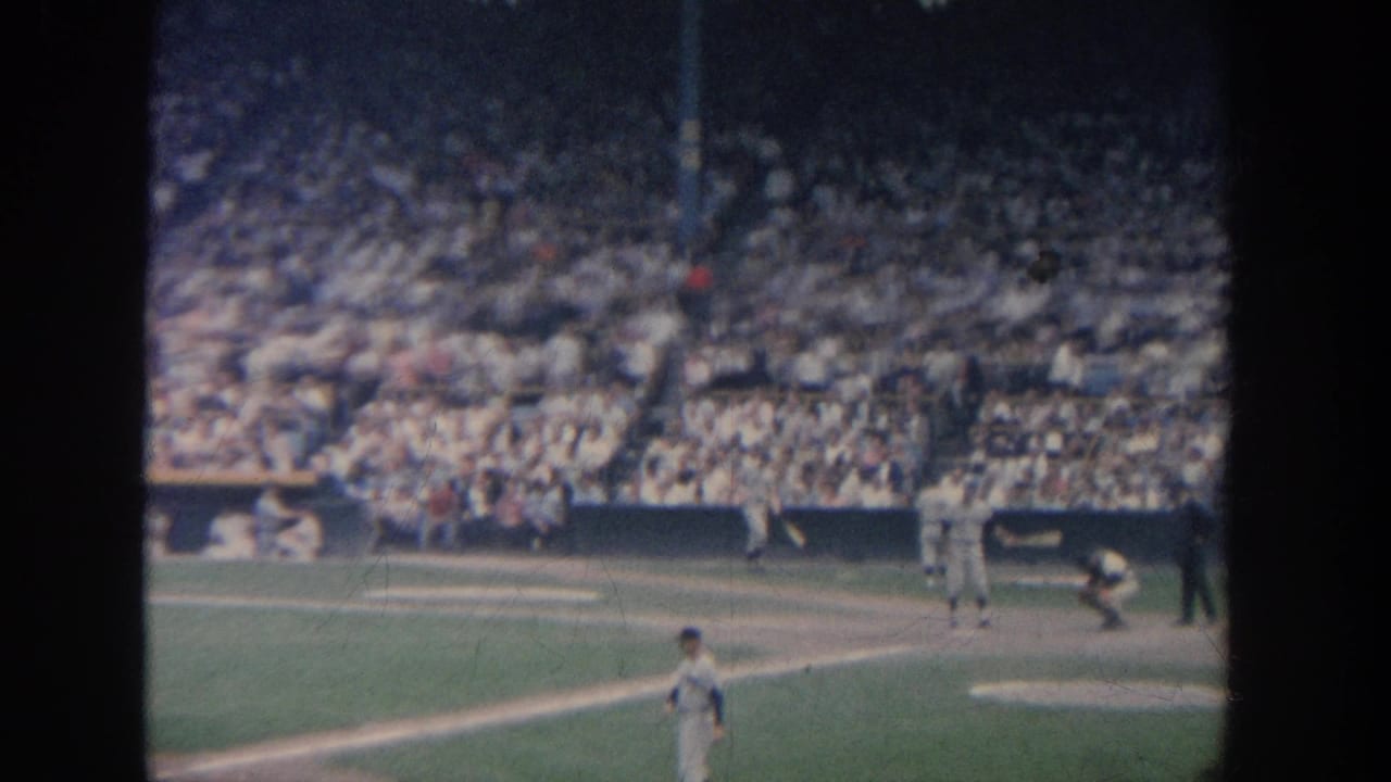1964 New York 8mm view of a baseball game with a batter at the plate, catcher crouched, fielders, and crowded stadium seating.