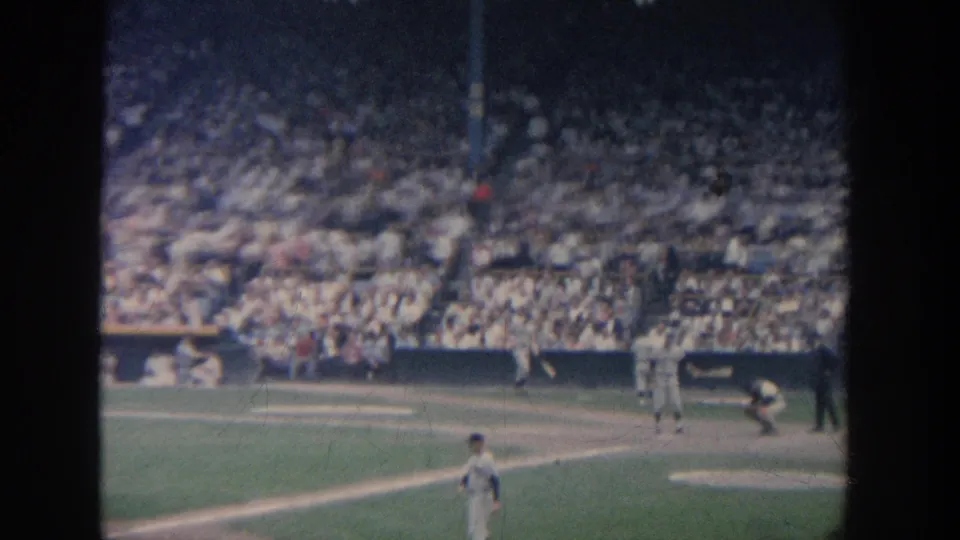 1964 New York 8mm view of a baseball game with a batter at the plate, catcher crouched, fielders, and crowded stadium seating.