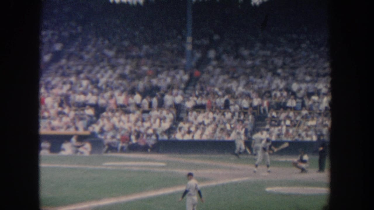 Baseball field with batter, catcher, several players, and spectators filling the stands.