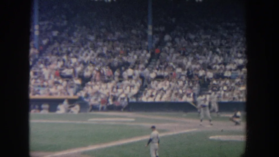 1964 New York 8mm stadium view with baseball players near the infield and a large crowd seated behind the field.