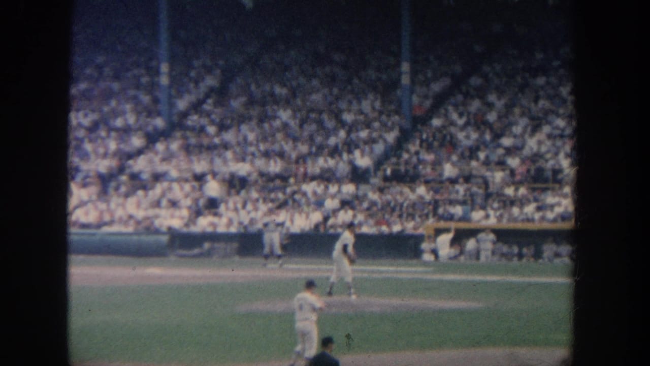 Baseball pitcher faces home plate as a batter, catcher, umpire, and large crowd are visible.
