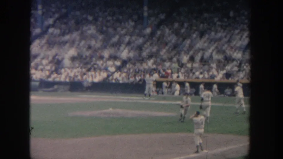 1964 New York stadium view showing a batter, several fielders, dugout area, and spectators in soft 8mm color.