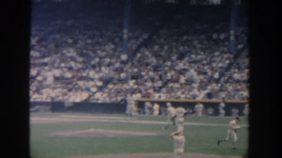 Wide 1964 New York baseball frame with players around the infield, a crowded grandstand, and visible 8mm frame masking.