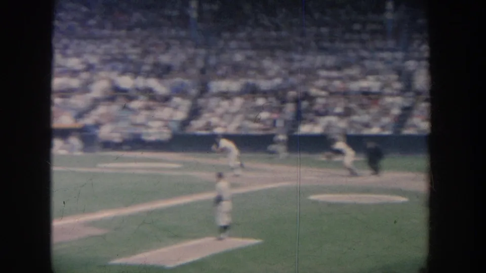 1964 New York baseball frame showing a runner on the first-base line, infield players, and a packed stadium crowd in soft 8mm focus.