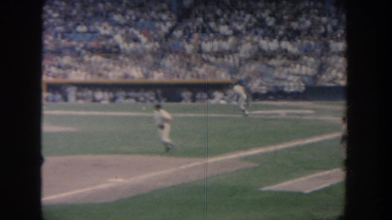 1964 New York 8mm view of baseball players on the field before packed stands, partly obscured by dark vertical frame edges.