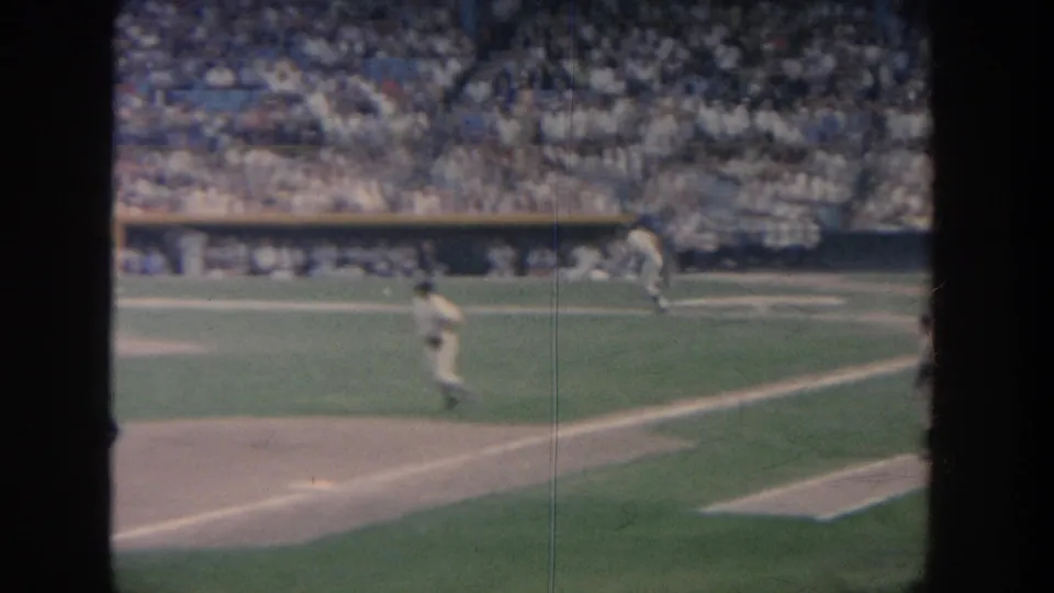 1964 New York 8mm view of baseball players on the field before packed stands, partly obscured by dark vertical frame edges.