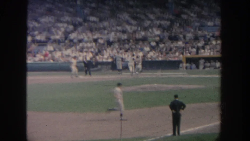 1964 New York stadium scene with players near the batter area, an official in dark clothing, and dense spectators in the background.