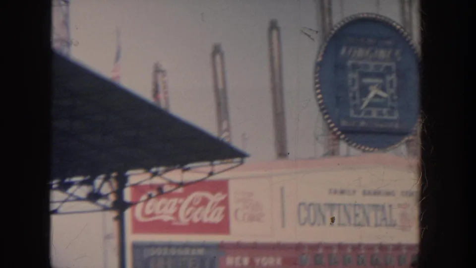 1964 New York stadium signage view with Coca-Cola branding, a Longines clock, and partial scoreboard or advertisement panels.