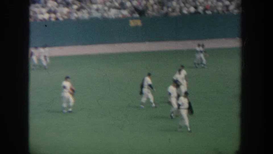 1964 New York ballpark field shot showing several baseball players in white uniforms walking near the outfield wall with spectators filling the background stands.