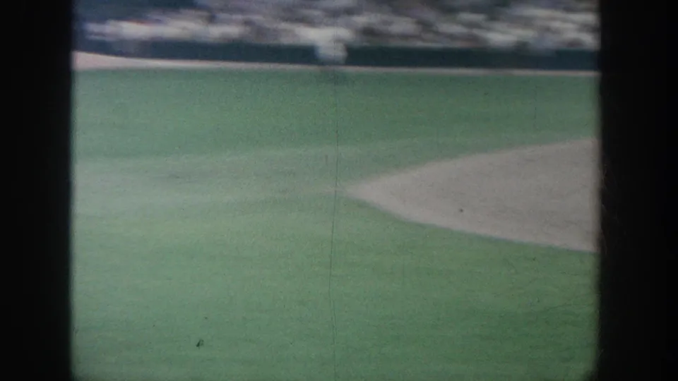 Soft 8mm view of a New York baseball field, with green grass, an infield edge, distant stands, and heavy dark frame borders.