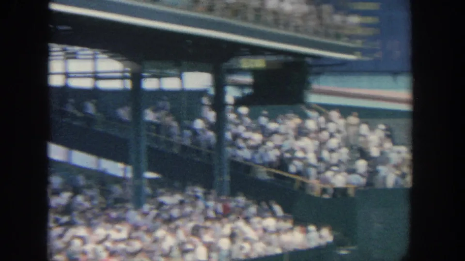 1964 New York baseball stadium crowd seen under an overhang, with spectators packed into shaded seating near the field wall.