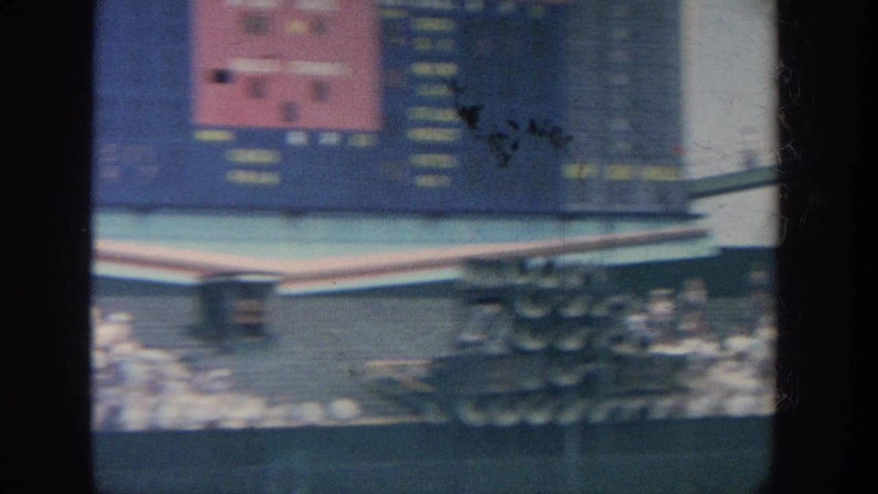 Blurred stadium scoreboard above crowded seating and part of the baseball field.
