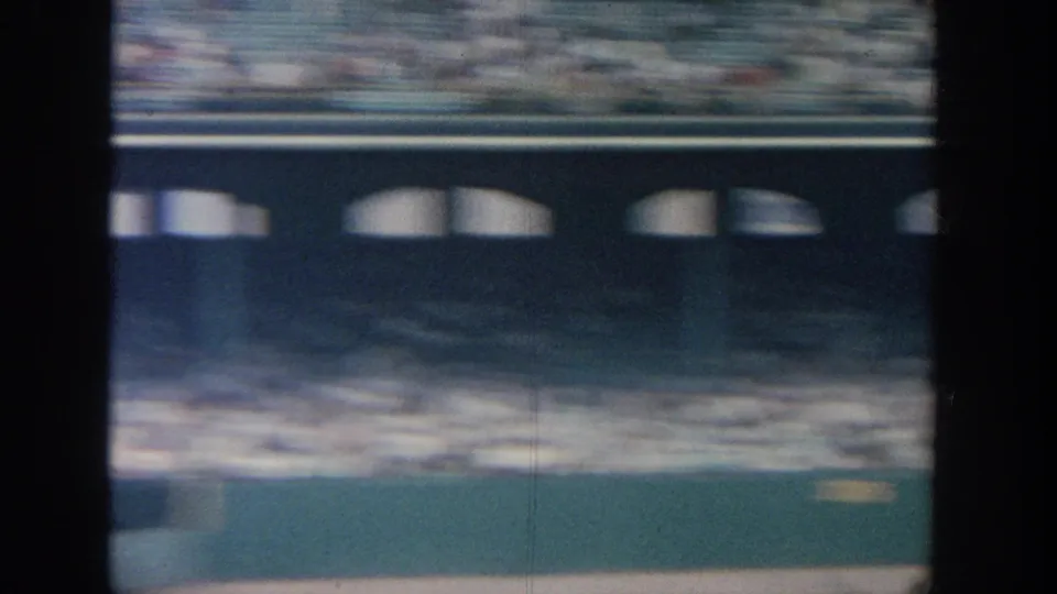 A 1964 New York ballpark view shows upper seating, dense spectators, and the outfield area through soft 8mm motion blur.