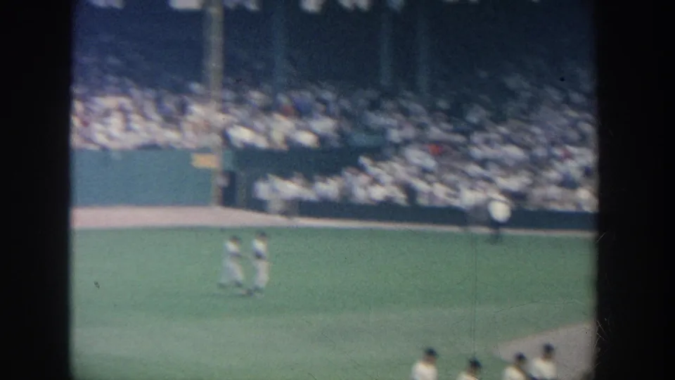 White-uniformed baseball players move across the field before packed stands in this 1964 New York 8mm home-movie frame.