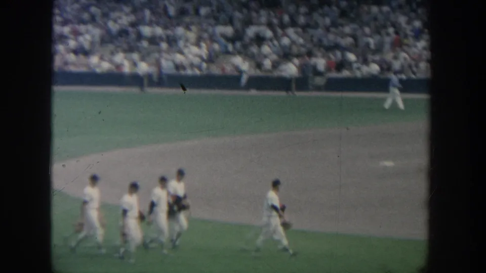 A group of white-uniformed players walks near the infield dirt as the crowded New York stadium remains visible in the background.