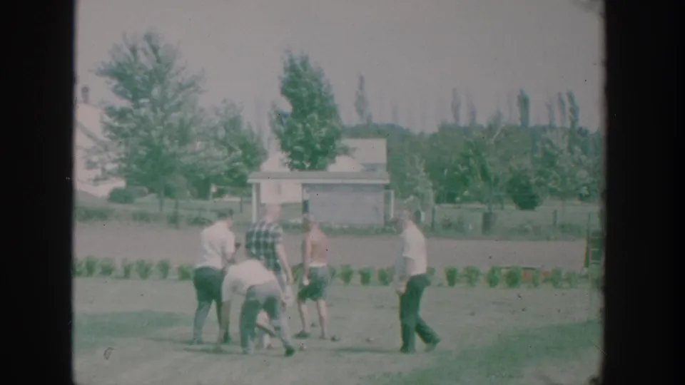 Men in casual shirts gather and bend near bocce balls on a residential lawn in 1964 New York home-movie footage.