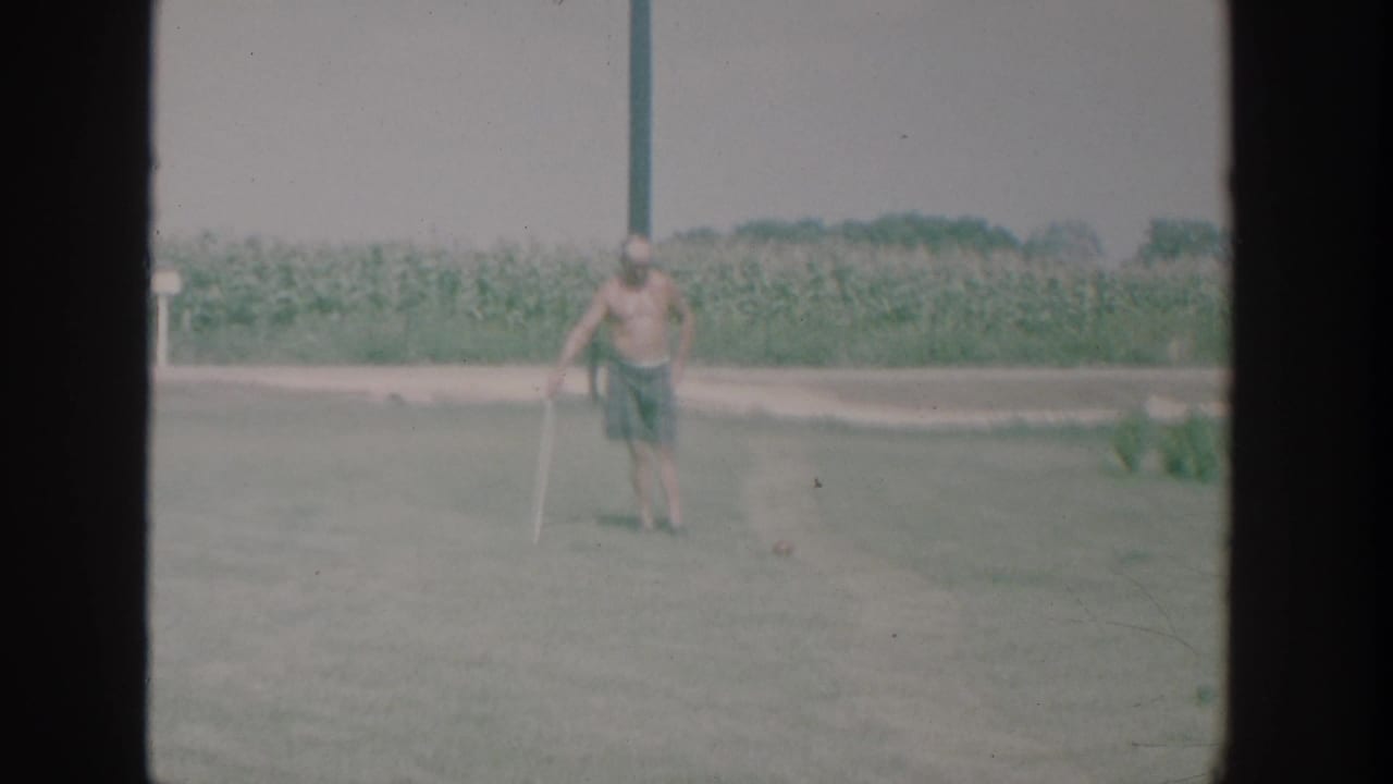Man on a lawn swings or leans with a croquet mallet near a small ball.