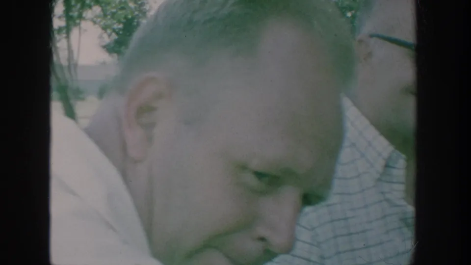 Close 1964 home-movie view of adults gathered outdoors, including a foreground man's face and another person partly visible beside him.