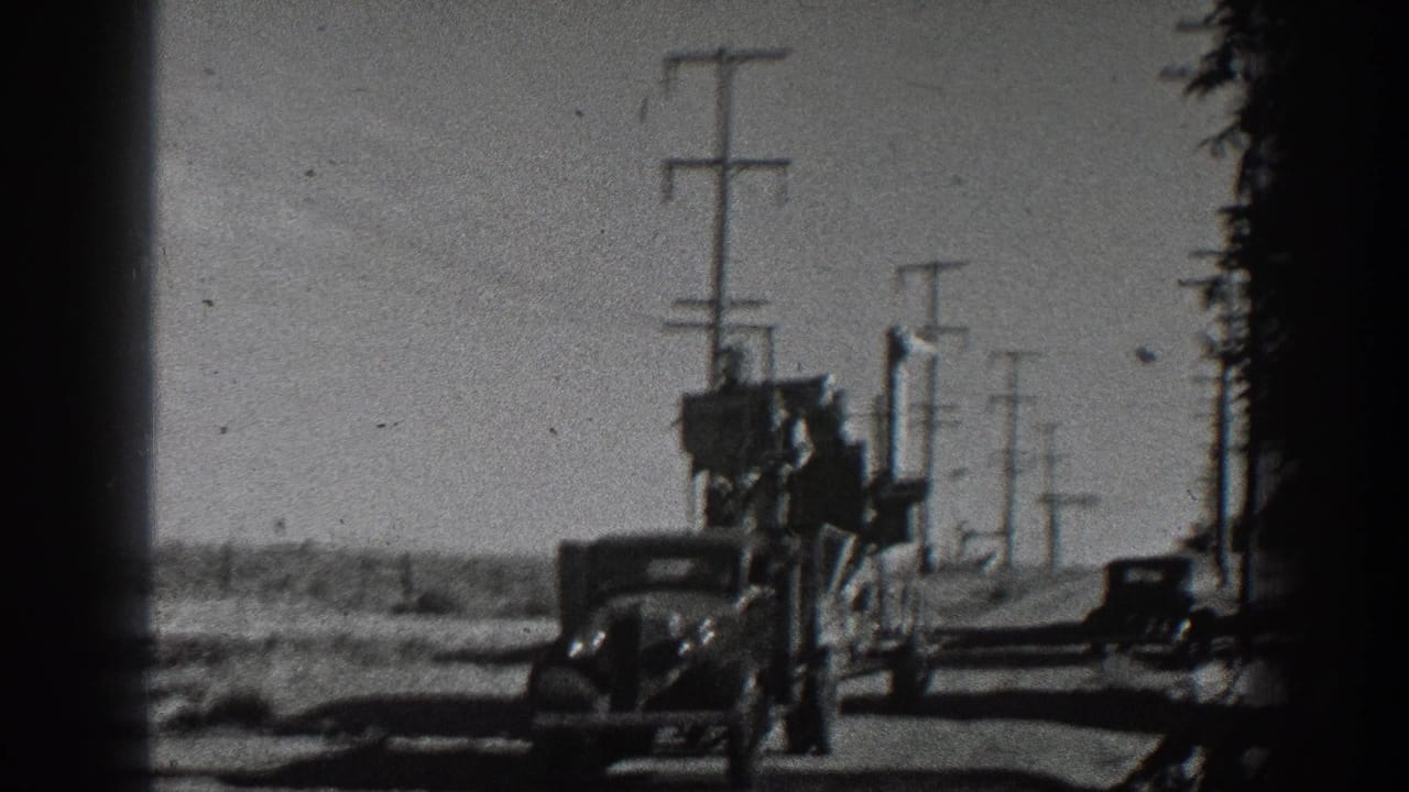 1936 California 8mm frame of a classic car towing a loaded flatbed trailer past utility poles on an open rural road.