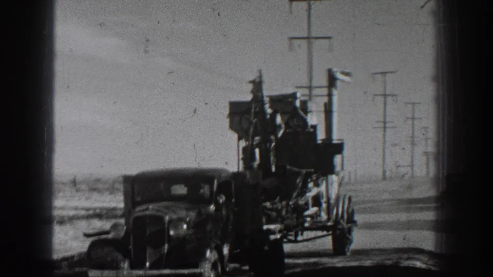 Close 1936 home-movie view of a classic car towing a tall, packed trailer, with a man visible among the load.