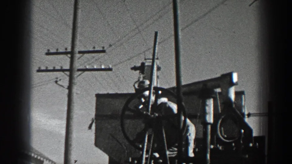 1936 California 8mm frame showing a large industrial wheel mechanism beside utility poles and overhead wires.