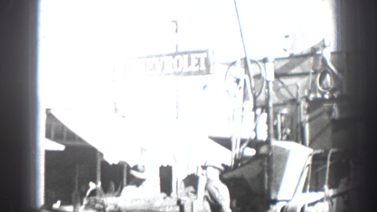 Overexposed street view with Chevrolet signage, parked vehicles, and figures near a garage area.