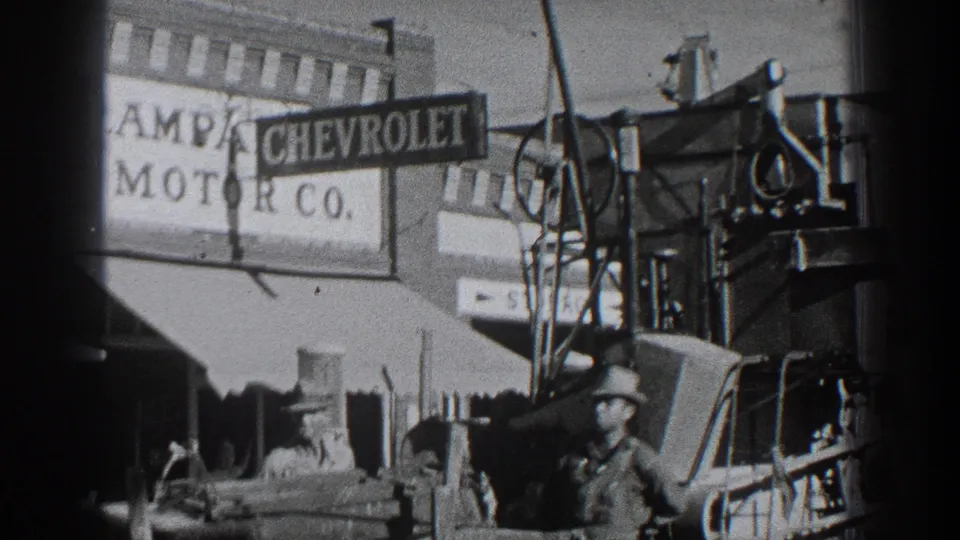 Black-and-white 1936 California frame with Lampa Chevrolet Motor Co. signage, older cars, equipment, and men in work clothes and hats near the dealership frontage.