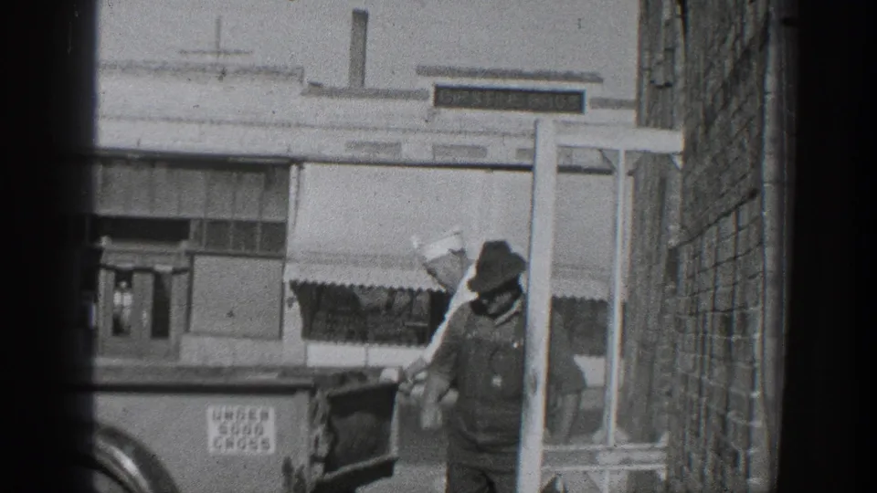 1936 California 8mm frame showing two men beside a truck in an alley, with storefront windows, an awning, and an UNDER 5000 GROSS sign visible.