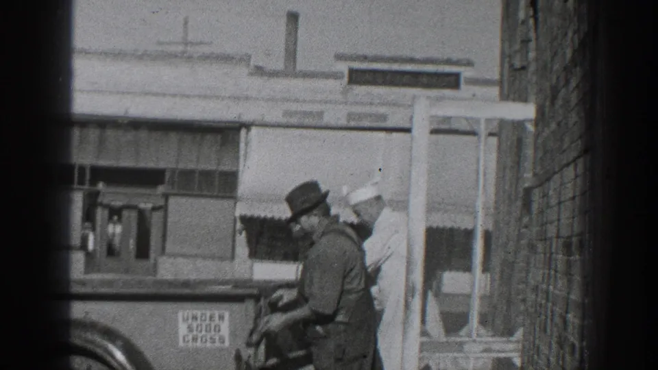 1936 California frame with a man in overalls and a brimmed hat at the truck, while a second man in a white cap and uniform stands nearby.