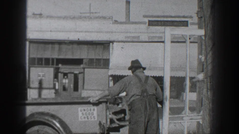1936 California frame showing a man seen from behind at the truck, with a second partly visible figure near the edge and storefront details beyond.