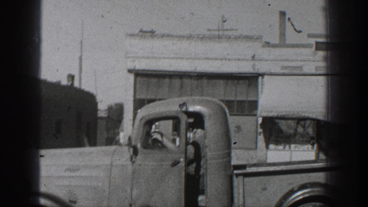 1936 California frame showing an older truck cab with an occupant, filmed from a home-movie viewpoint near building fronts.