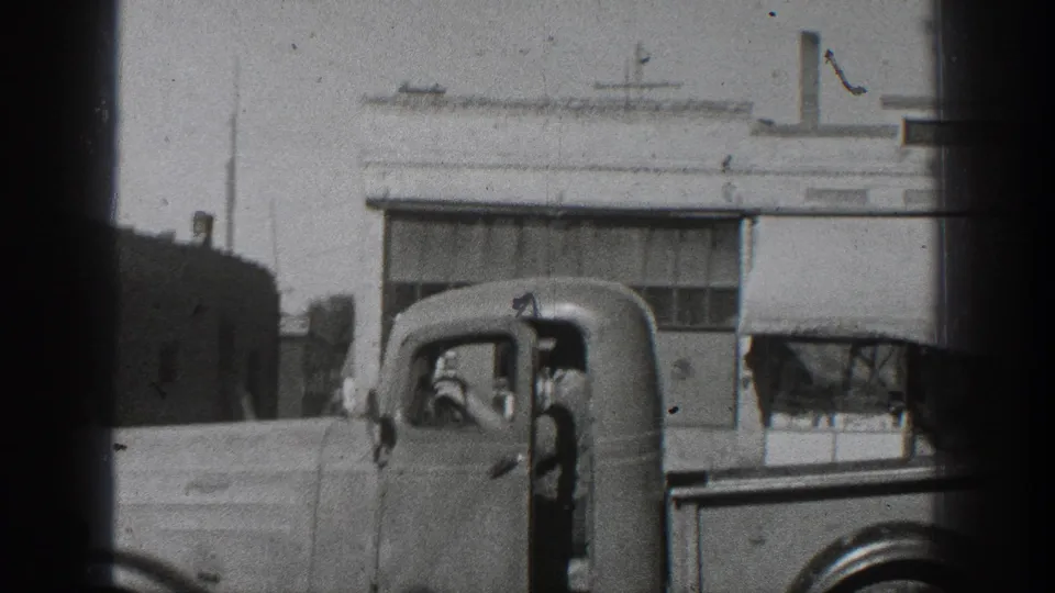 1936 California frame showing an older truck cab with an occupant, filmed from a home-movie viewpoint near building fronts.