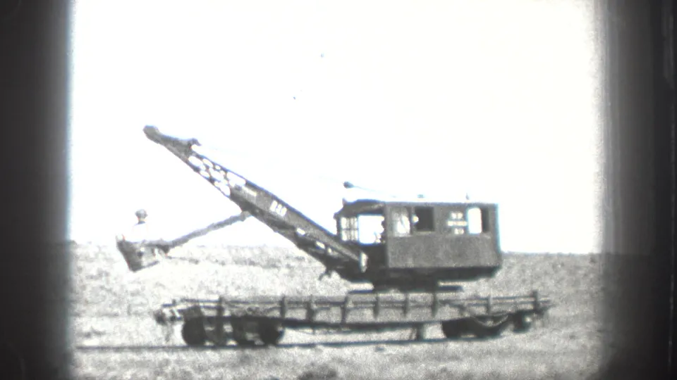 1936 California frame showing a large crane or excavator on a rail or flatbed platform in an open field.