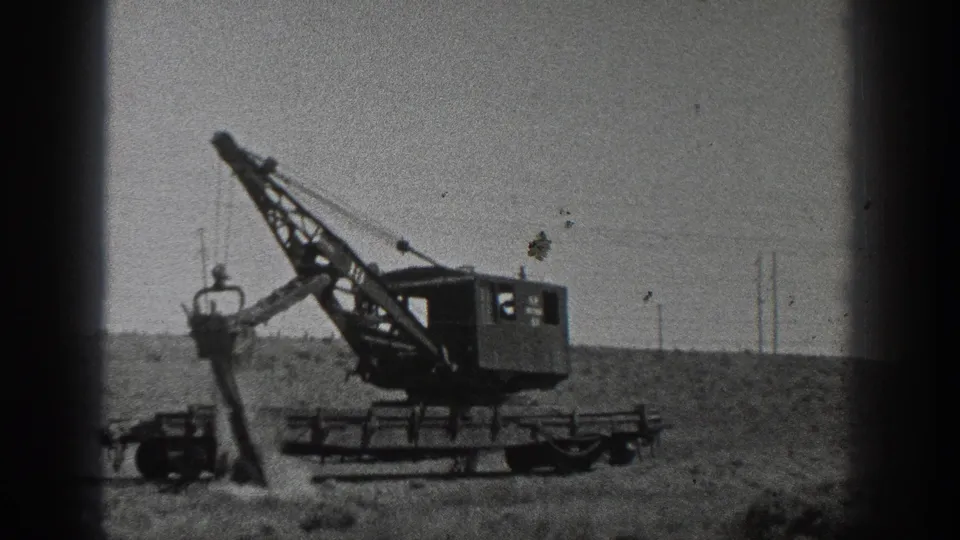 1936 California 8mm frame of a crane lifting or dumping soil beside its wheeled chassis in an open landscape.