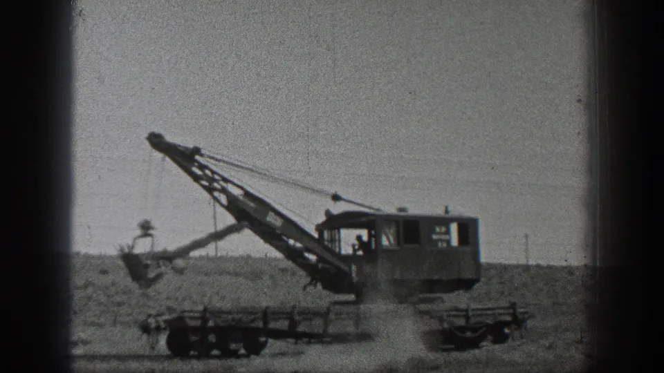1936 California 8mm frame showing an operator inside a crane cab as the machine works over a dusty field.