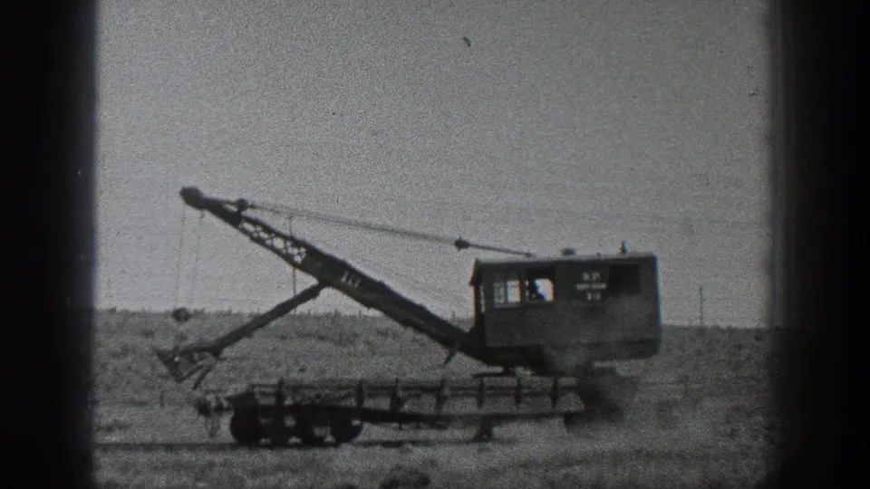 1936 California 8mm frame of a wheeled crane finishing a dirt-moving pass in an open field.