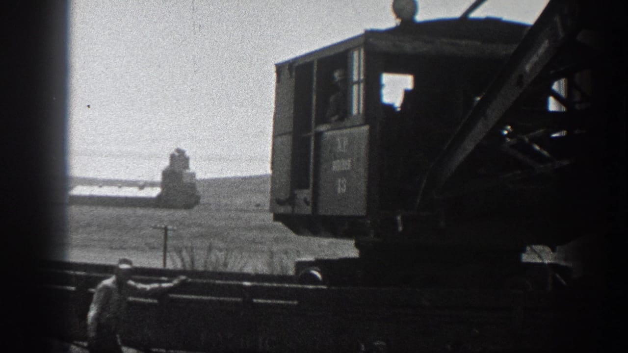 Rail-mounted crane equipment appears in silhouette against a bright open California landscape, with a worker near the lower frame.