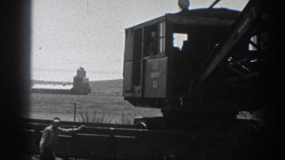 Rail-mounted crane equipment appears in silhouette against a bright open California landscape, with a worker near the lower frame.