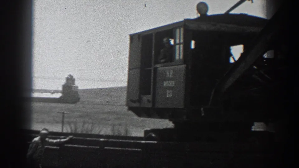 The 8mm frame shows the crane cab, boom structure and a worker below, with flat terrain visible behind the machinery.