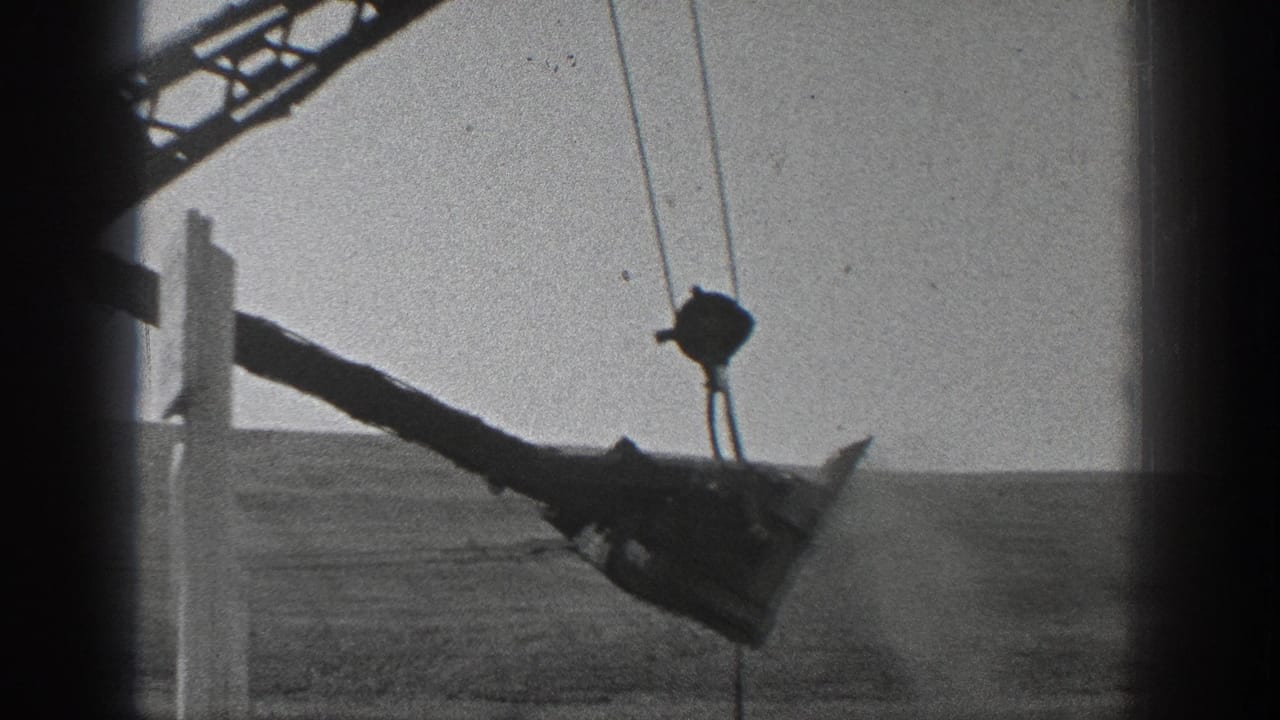 1936 California 8mm frame showing a cable-operated crane arm and suspended bucket beyond a dark passing window frame.