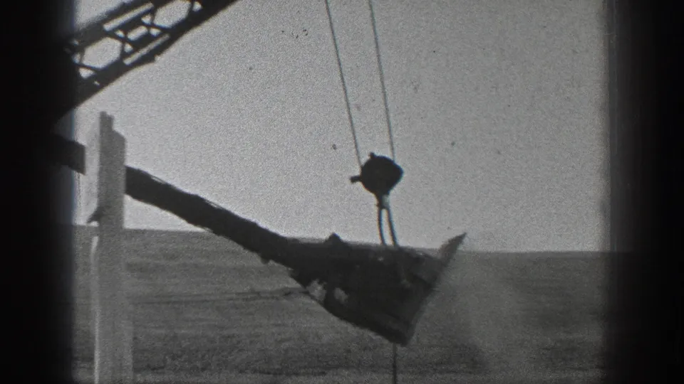 1936 California 8mm frame showing a cable-operated crane arm and suspended bucket beyond a dark passing window frame.