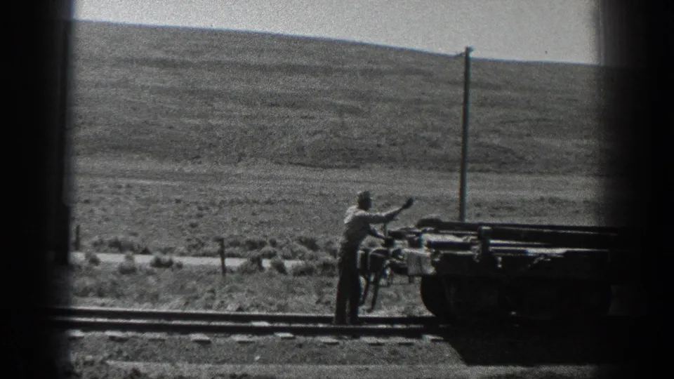 1936 California frame showing a worker near rail tracks and heavy machinery, with low hills and utility poles behind him.