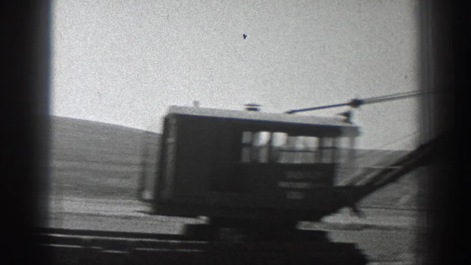 Motion-blurred 1936 California 8mm frame of a rail-side machinery cab passing the camera beneath overhead cables.