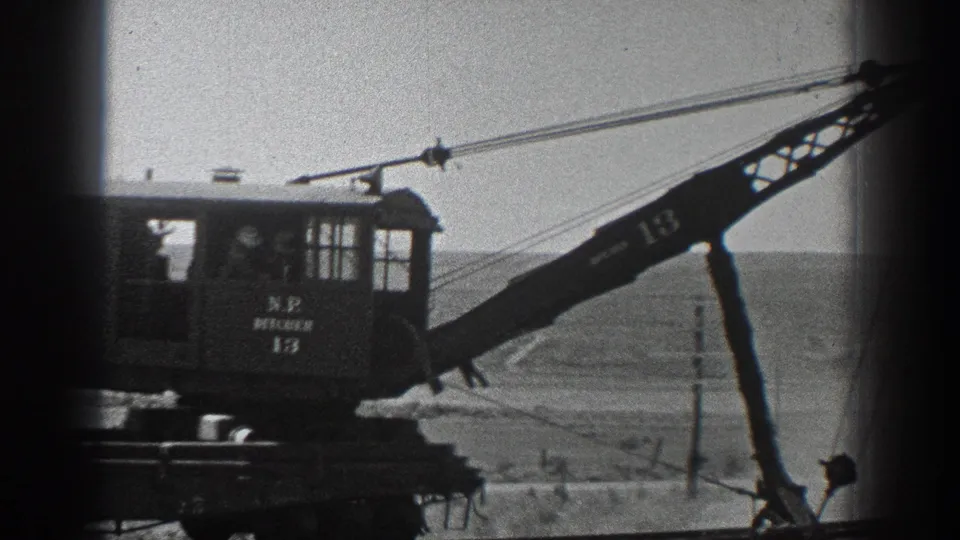 Marked rail crane cab and boom seen in black-and-white 8mm footage from the California railway construction scene.